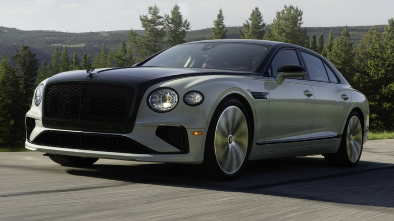 A two-tone Bentley Flying Spur driving on the road surrounded by trees