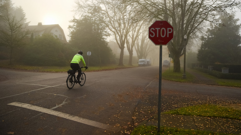A man on a bicycle in a bright lime green jacket passing intersection with a stop sign