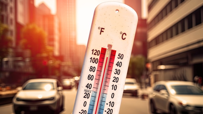 Thermometer showing high temperature with cars in the background