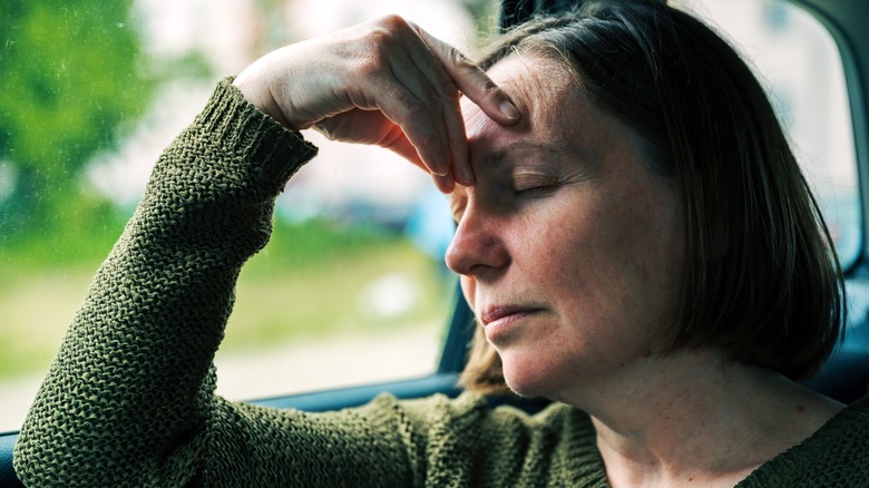 Person with hand against forehead in a car.