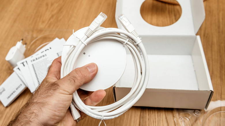 person holding a white ethernet cable with a box in the background on a wooden surface