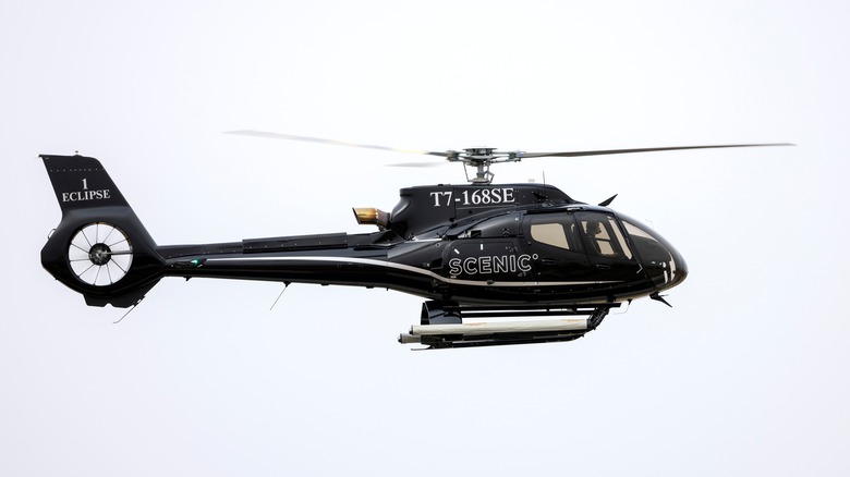 An Airbus H130 helicopter hovering in the air with SCENIC branding on it.