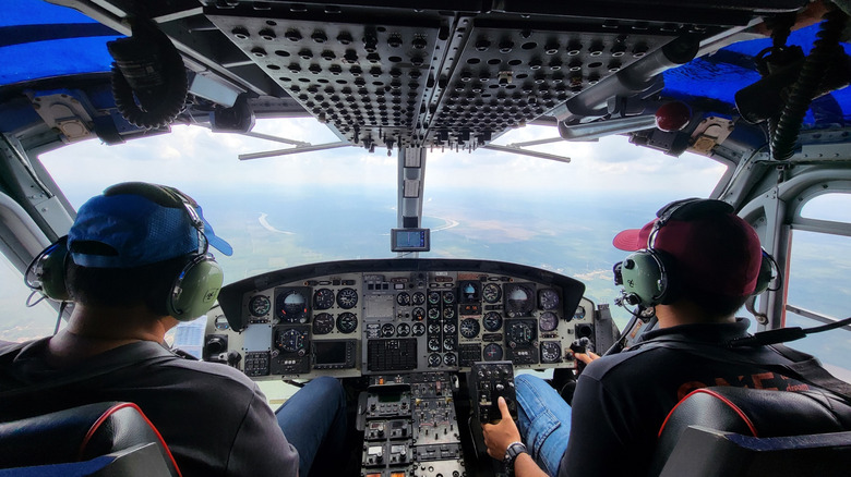 Photo from behind of an army helicopter cockpit with a pilot and passenger while flying.