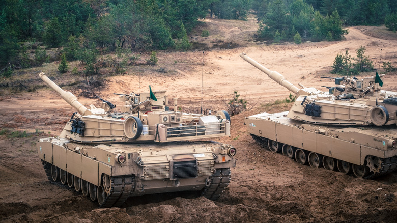 Two M1 Abrams tanks during exercise in muddy clearing in woods