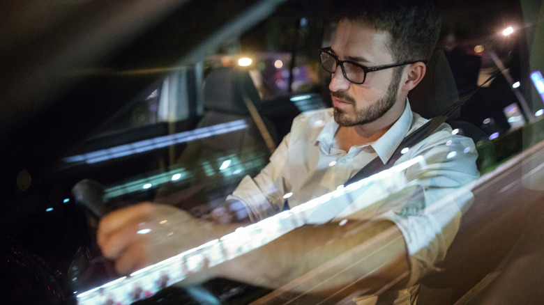 A man in glasses driving city streets at night