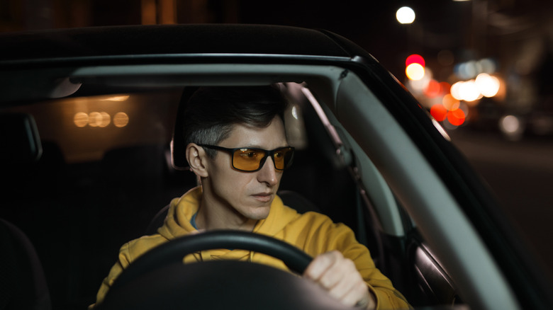 A man driving a car at night while wearing yellow-tinted night driving glasses