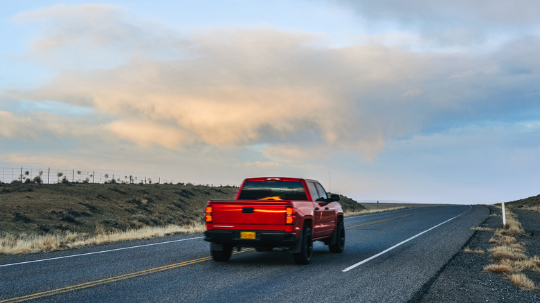 Lone red pickup truck driving down road in the morning