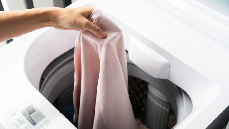 person putting clothes in a white washing machine