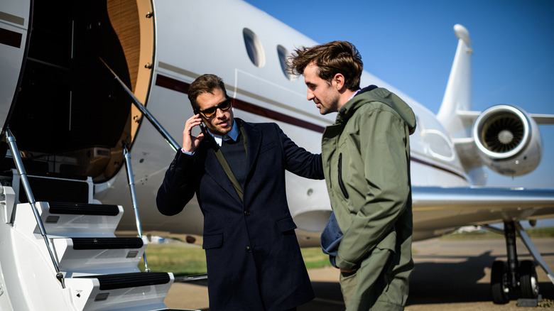 Two men standing beside a private jet, with one of them talking on the phone and wearing sunglasses