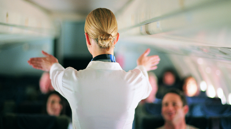 A Flight attendant in  white uniform giving safety demonstration on plane