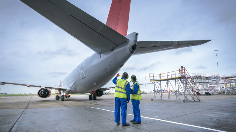 Workers in hi-visibility vests looking at plane on tarmac