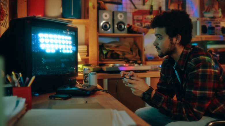 A person playing Space Invaders on a CRT TV in a room full of tools and gadgets.