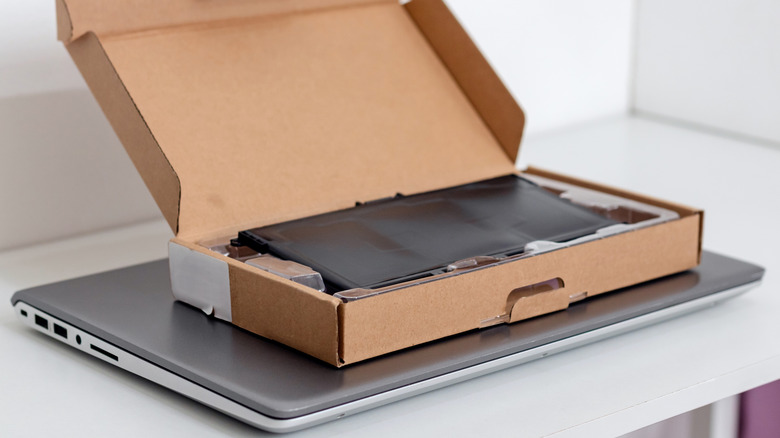 Laptop on table with box with new battery on top