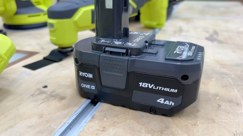 A close-up of a Ryobi 18V ONE+ battery attached to an unidentified tool, other Ryobi tools in the background