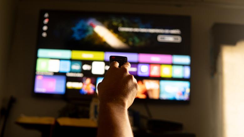 A person pointing a remote towards a smart TV with menu icons visible