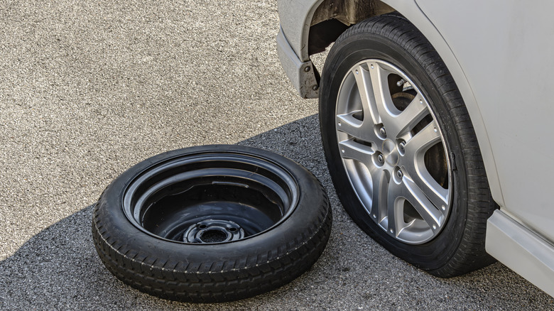 Spare tire on the ground next to a blown tire on the car