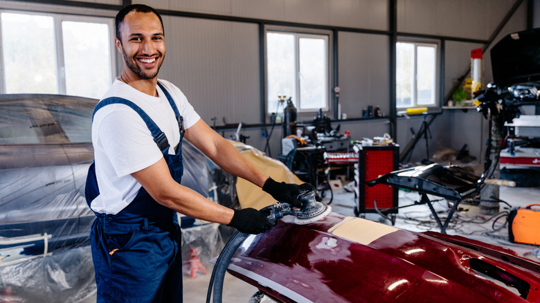 A professional mechanic in a body shop polishing a car's bumper.