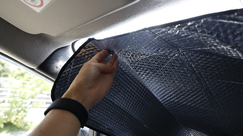 A person attaching a sunshade to their car windshield.