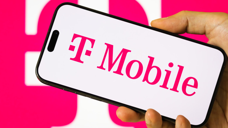 A person holds a smartphone displaying the logo of T-Mobile US Inc
