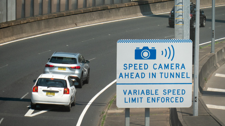 Speed camera warning sign on highway reading, "Speed Camera Ahead in Tunnel Variable Speed Limit Enforced"