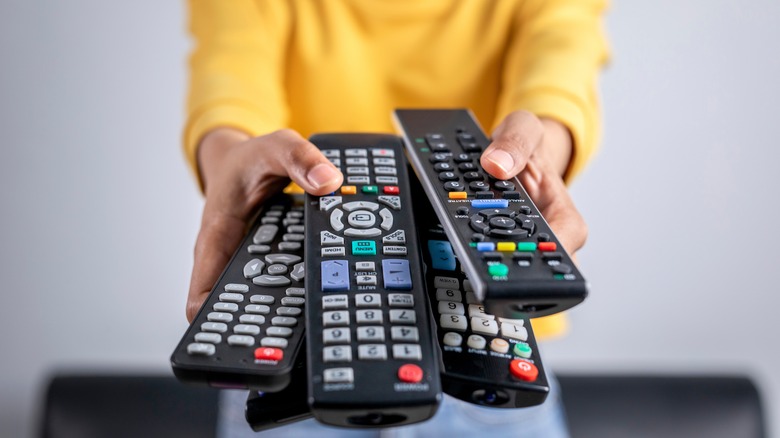 A woman in a yellow top holding out a handful of TV remotes