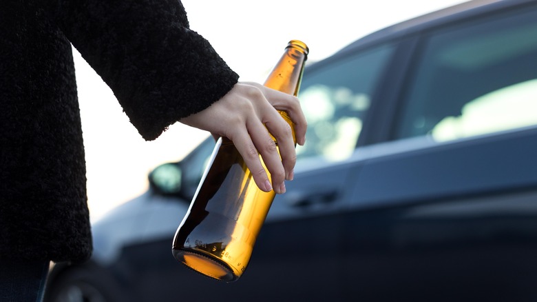 Person holding beer bottle in front of car