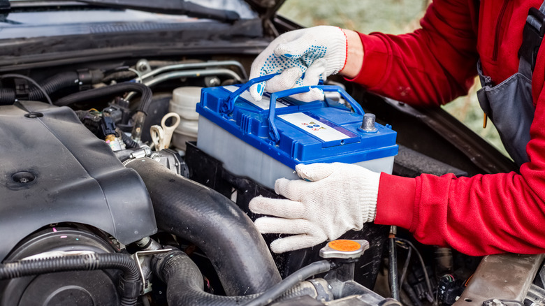 A car mechanic installing a new battery in a car.