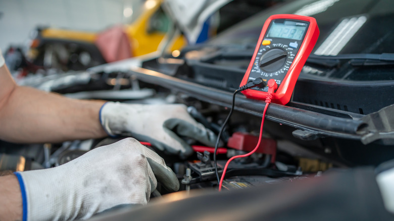 Car mechanic checking voltage of a car battery using a multimeter.