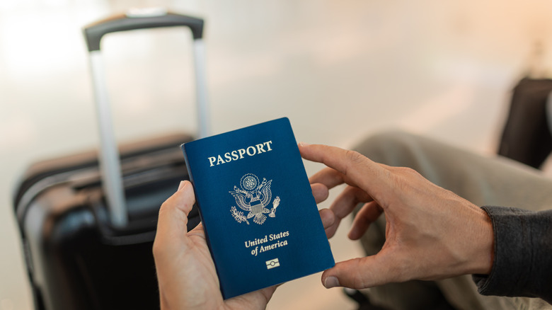 Man holding passport in hand with luggage in the background