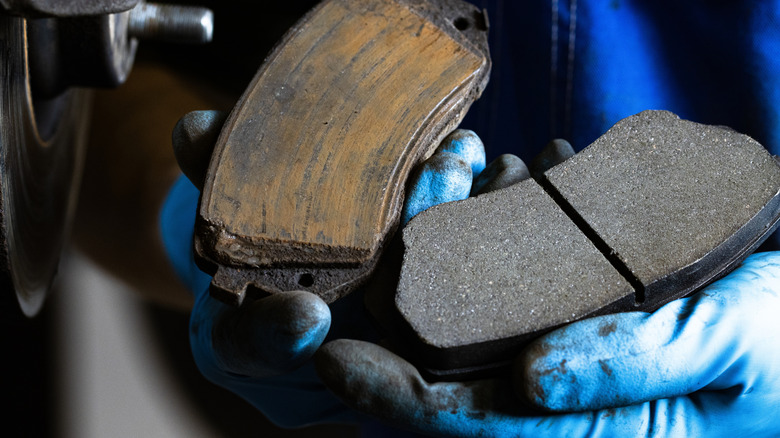 Close-up of new and old brake pads held in blue-gloved hands
