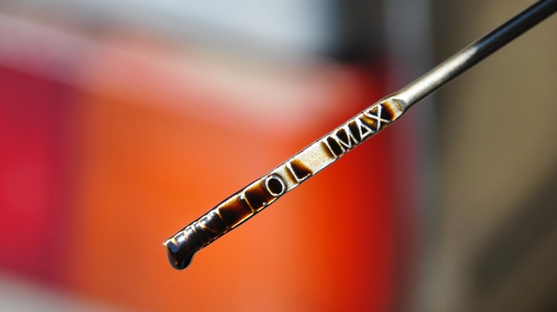An engine oil dipstick with very dirty, dark-colored oil