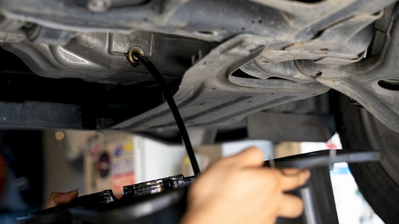 A person draining old very dark engine oil from a vehicle