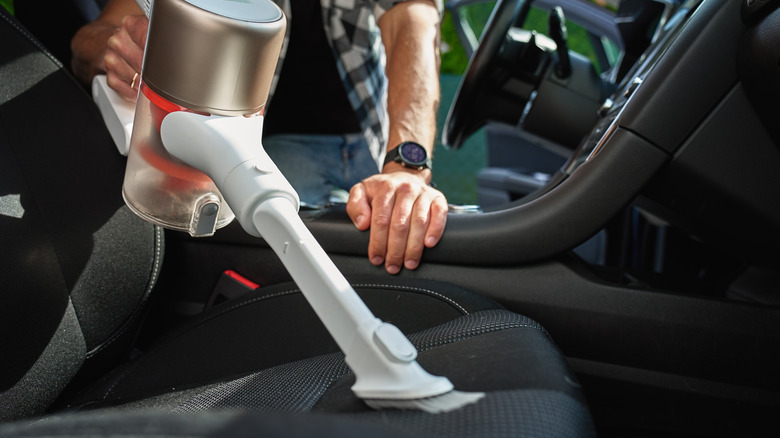 Person cleaning car interior with small vacuum.