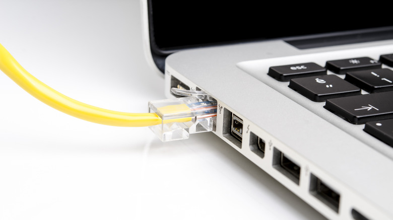 A yellow ethernet cable plugged into a laptop placed on a white surface