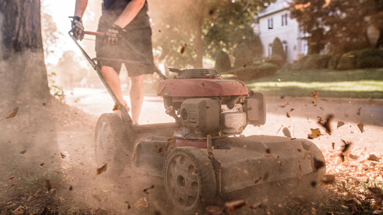 A lawn mower in operation, kicking up stones and debris
