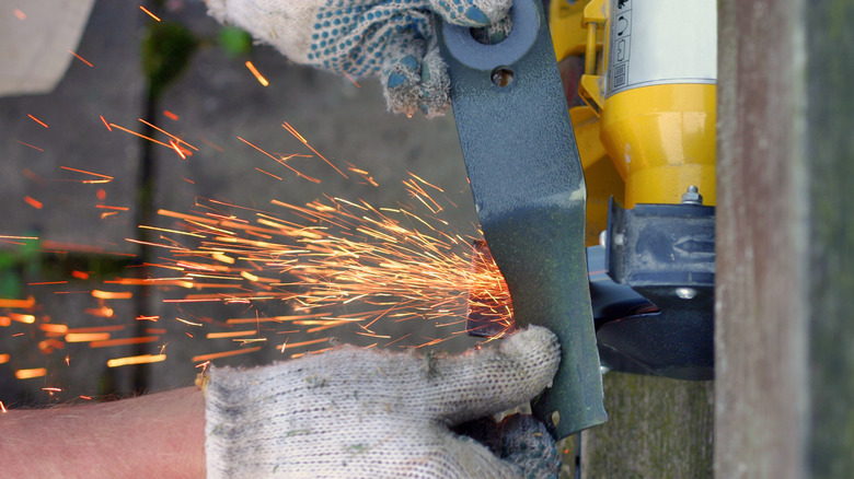 Close up of hands holding a lawn mower blade against a grinding wheel