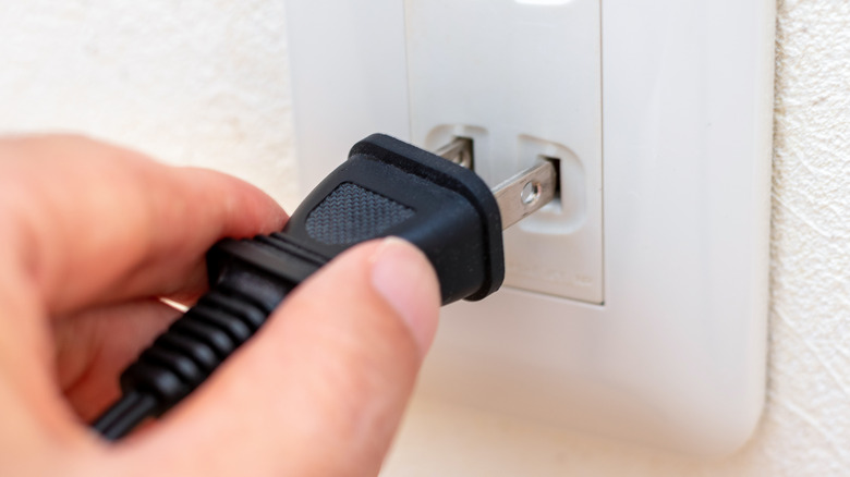 A person holding a plug inside a wall outlet.