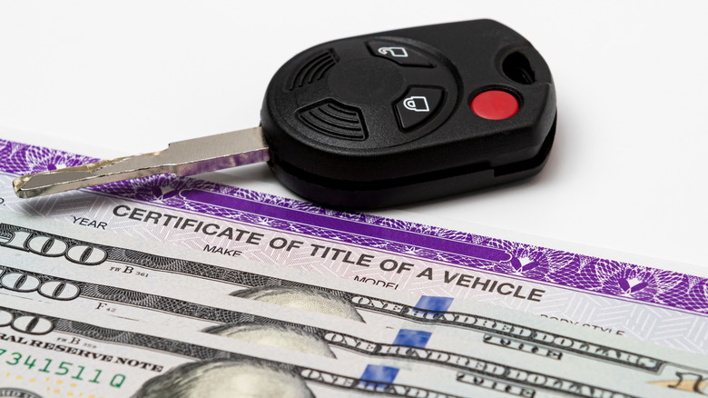 A car key, with a vehicle title, and cash.