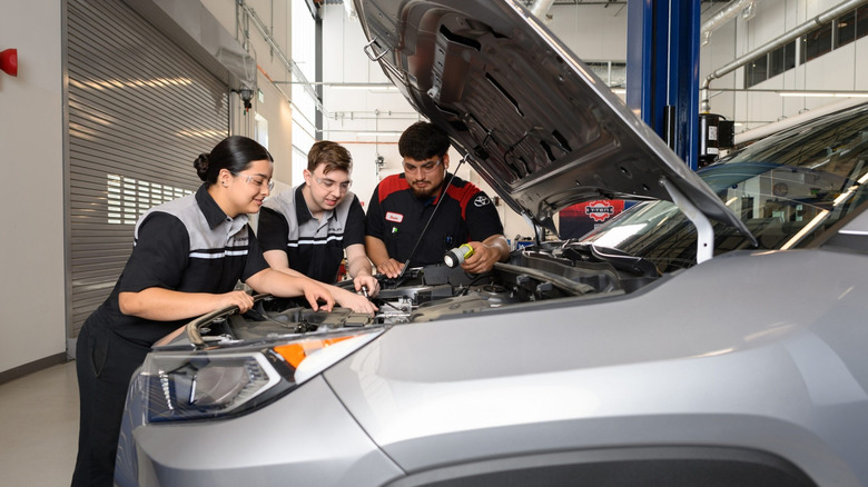 Technicians working under the open hood of a car