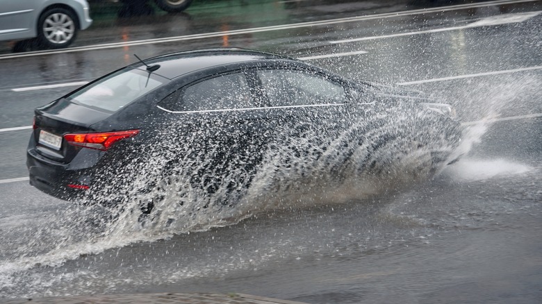 Car splashing water, driving through puddle at heavy rain.