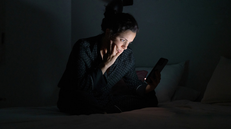 Woman in bed appearing to be doom-scrolling at night.