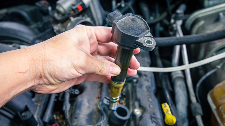 A person holding an ignition coil taken out of a dirty engine