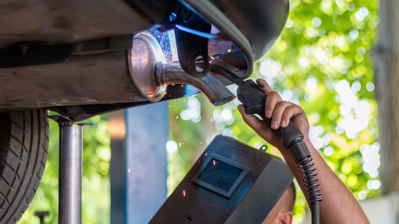 Mechanic servicing exhaust system with a welder