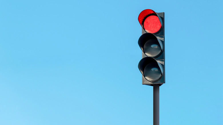 Modern traffic light with red light in front of cloudless sunny blue sky