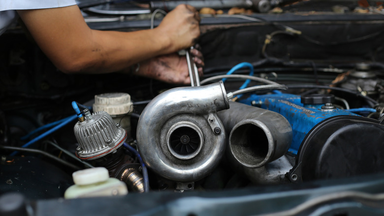 A mechanic working on a turbocharged car, turbocharger front and center with one of the pipes detached