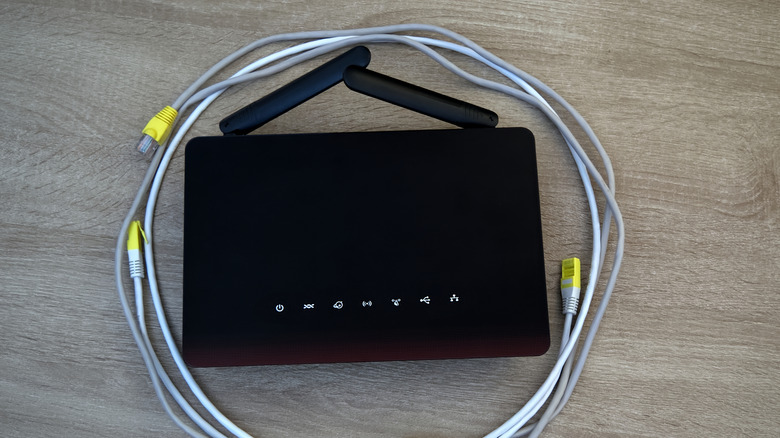 A router with two grey ethernet cable circling it against a wooden background