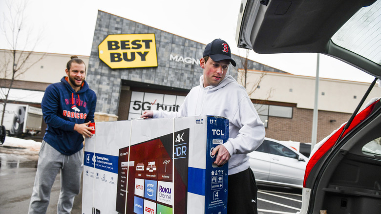 Shoppers loading a TV into a car outside a Best Buy store