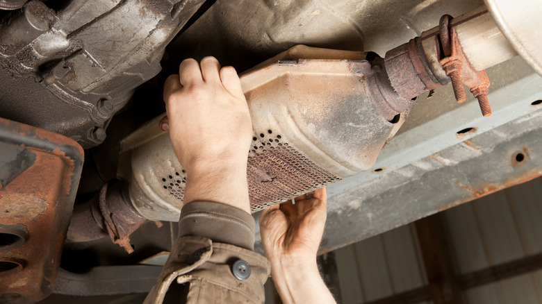 Mechanic hands removing Catalytic Converter from under a car