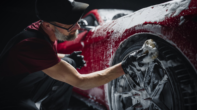 A man wearing a black cap cleaning a red car