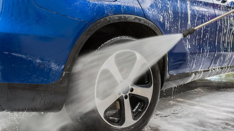 Cleaning a blue car using a pressure washer.